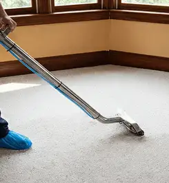 Steam carpet cleaning technician using a hot-water extraction wand on a residential carpet, wearing blue protective shoe covers Chandler, AZ.